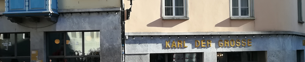 Teil der Fassade des Gebäudes Kirchgasse 14 in Zürich mit der goldenen Aufschrift "KARL DER GROSSE". Eigene Fotografie.