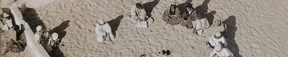 Luftaufnahme eines Innenhofes eines algerischen Gebäudes. Junge Muslime sitzen in einem Halbkreis im Sand. Ausschnitt aus Umschlagfoto von Henriette Grindat: Algérie, 1956.